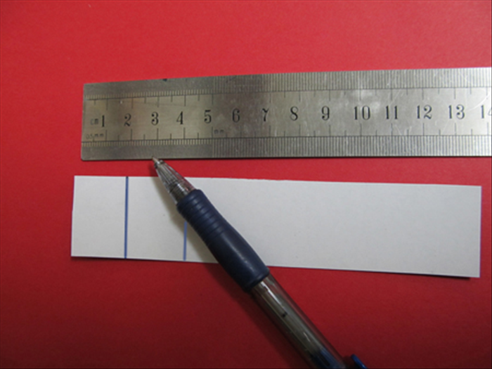 חתכו את הנייר הלבן העבה או הקרטון הלבן הדק לחתיכה בגודל 3X14 ס'מ.

בצד האחורי ציירו קו 2 ס'מ מלמעלה ועוד קו 4 ס'מ מלמעלה.